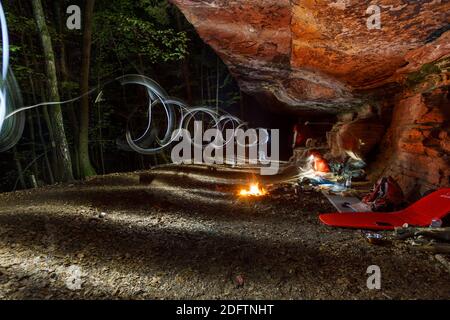 Lagerfeuer am Campingplatz unter roten Felsen im pfälzerwald bei Nacht mit Lichtmalerei Stockfoto