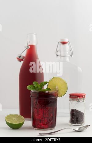 Flasche und Tasse medizinischen Hibiskustee und getrocknete Hybiskusblätter in transparentem Glas auf weißem Hintergrund, garniert mit Limettenscheiben und frisch Stockfoto