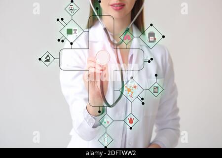 Junge Ärztin mit Stethoskop mit virtuellen Bildschirm auf grauem Hintergrund. Konzept moderner Technologien in der Medizin Stockfoto