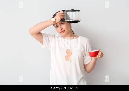 Gestresste junge Frau mit Kaffeeflecken auf ihrem T-Shirt Weißer Hintergrund Stockfoto