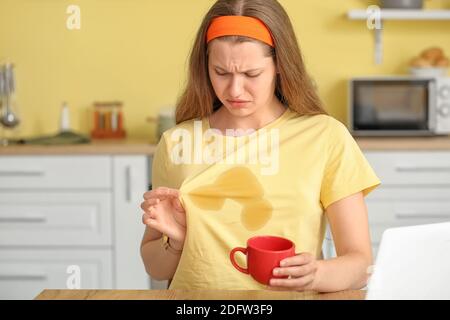 Gestresste junge Frau mit Kaffeeflecken auf ihrem T-Shirt in Küche Stockfoto