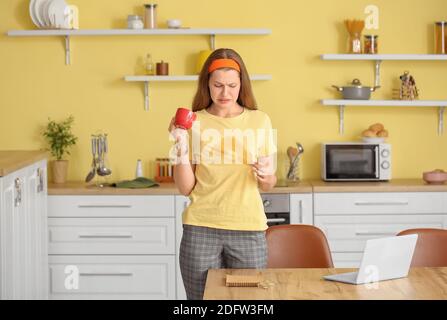 Gestresste junge Frau mit Kaffeeflecken auf ihrem T-Shirt in Küche Stockfoto