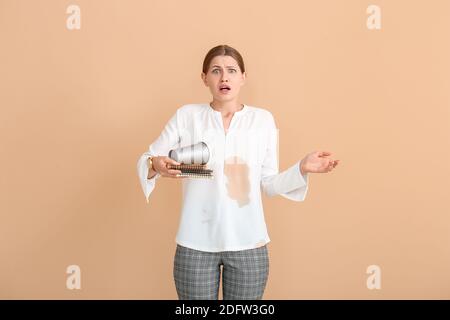 Gestresste junge Frau mit Kaffeeflecken auf ihrem Hemd Farbiger Hintergrund Stockfoto
