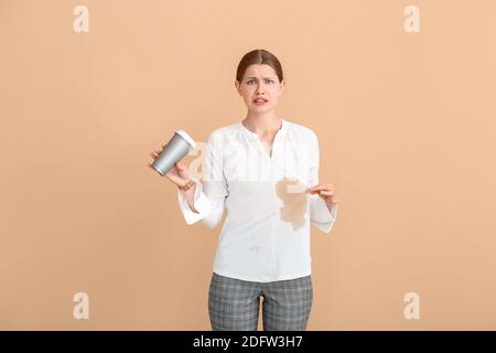 Gestresste junge Frau mit Kaffeeflecken auf ihrem Hemd Farbiger Hintergrund Stockfoto