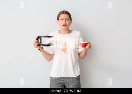 Gestresste junge Frau mit Kaffeeflecken auf ihrem T-Shirt Weißer Hintergrund Stockfoto