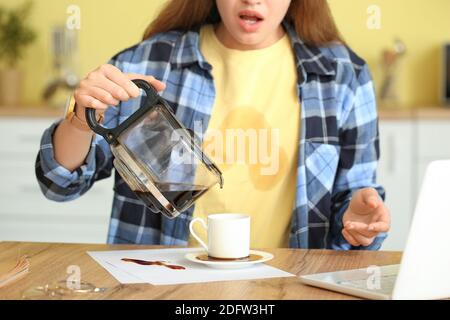 Gestresste junge Frau mit Kaffeeflecken auf ihrem T-Shirt und Verschütteter Kaffee in der Küche Stockfoto