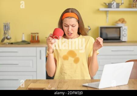 Gestresste junge Frau mit Kaffeeflecken auf ihrem T-Shirt in Küche Stockfoto