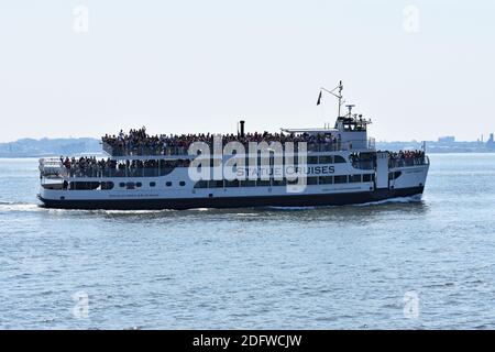 Ein vollgepacktes Boot voller Kameras, das Besucher von Statue Cruises hält, fährt zur Freiheitsstatue im Hafen von New York City, USA. Stockfoto