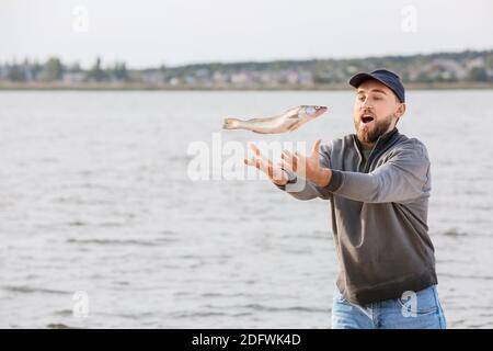 Junger Mann mit gefangenem Fisch in der Nähe des Flusses Stockfoto