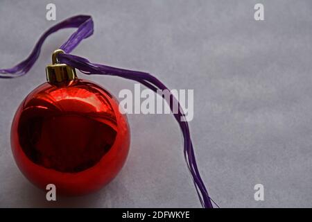 Eine große rote Weihnachtskugel mit violettem Band auf grauem Hintergrund mit Kopierraum. Stockfoto