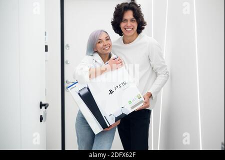Ein glückliches junges Paar ist gerade mit einer brandneuen PlayStation 5-Spielekonsole von Sony aus dem Geschäft nach Hause gekommen. Sie haben es bei einem Black Friday-Verkauf bekommen. Moskau - November Stockfoto