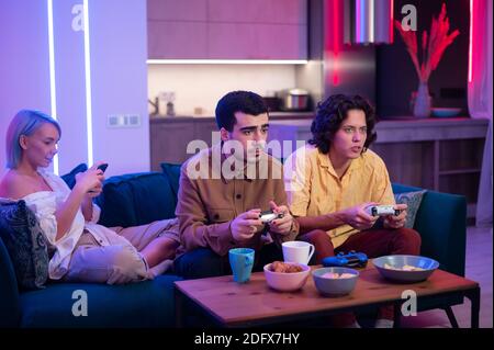 Freund eines jungen Paares kommt zu ihrem Haus, um Spiele auf Spielkonsole an angenehmen Abend zu spielen. Glückliche Menschen spielen Videospiele zu Hause. Heimparty Stockfoto