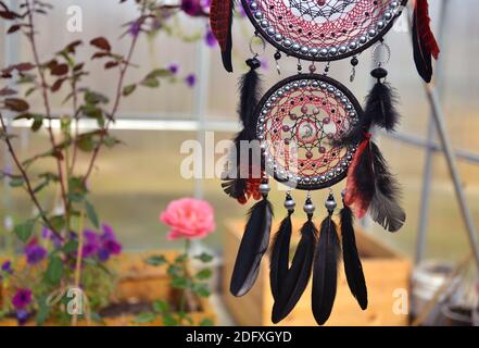 Schöner boho-roter und schwarzer Traumfänger mit Federn im Zigeunerstil. Mystischer natürlicher Hintergrund mit Traumfänger, esoterischem und okkulten Konzept Stockfoto