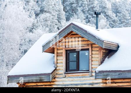 Nahaufnahme einer Mansarde Kunststoff-Fenster auf einem Landhaus, das Dach ist mit Schnee bedeckt, und vor dem Hintergrund eines verschneiten Waldes Stockfoto