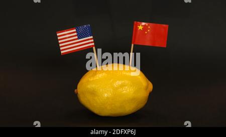 US- und chinesische Nationalflaggen stecken in der Haut einer leuchtend gelben Zitrone. Gefühlvolle, angespannte, bittere, angespannte internationale Beziehungssymbol. Stockfoto