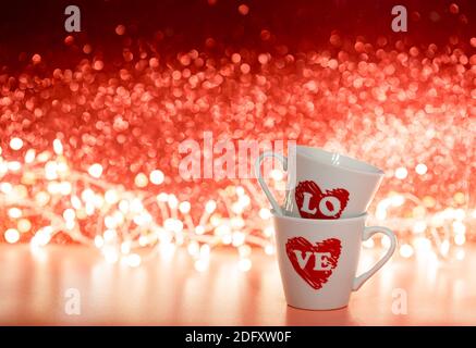 Valentinstag-Konzept mit weißen Kaffeetassen mit Liebe Text In Herzform auf rot glänzendem Hintergrund Stockfoto