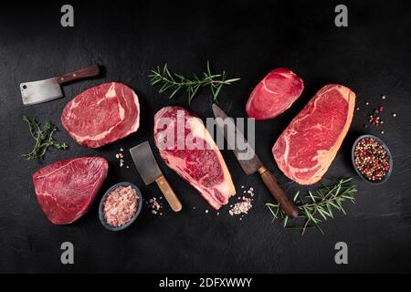 Fleisch flach legen. Verschiedene Fleischstücke, über Kopf flach lag Schuss mit Messern, Salz, Pfeffer und Kräuter, auf einem schwarzen Schiefer Hintergrund Stockfoto