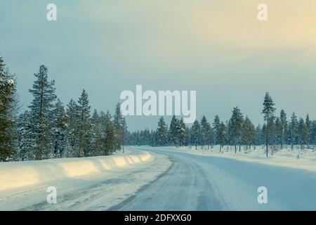 Winter Finnland. Seltener Nordwald und viel Schnee. Leere Autobahn mit Drifts auf der Seite. Schwaches Sonnenlicht Stockfoto