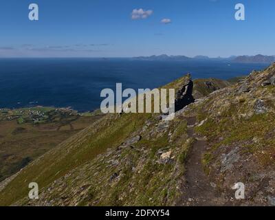 Exponierter Wanderweg am steilen Bergrand, umgeben von Felsen und Gras mit herrlichem Panoramablick über das Norwegische Meer an der Nordküste. Stockfoto