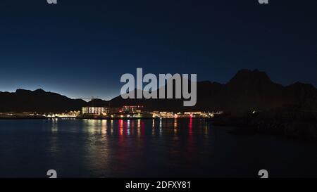 Atemberaubende Nachtansicht des Fischerdorfes Svolvær, Lofoten, Norwegen mit beleuchteten Gebäuden, die sich im ruhigen Wasser spiegeln, Holzstockfischregale. Stockfoto