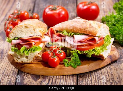 Zwei Sandwiches mit Schinken und Gemüse auf Holzbrett Stockfoto