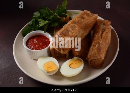 Jachnun oder Jahnun, jemenitisches jüdisches Gebäck, serviert mit frisch geriebenen Tomaten und gekochtem Ei und Zhug, aus den Adeni-Juden, und traditionell Stockfoto