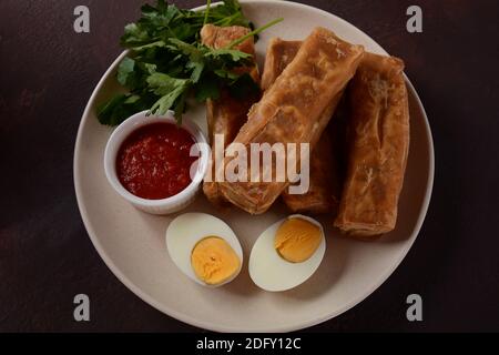 Jachnun oder Jahnun, jemenitisches jüdisches Gebäck, serviert mit frisch geriebenen Tomaten und gekochtem Ei und Zhug, aus den Adeni-Juden, und traditionell Stockfoto