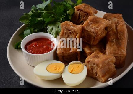 Jachnun oder Jahnun, jemenitisches jüdisches Gebäck, serviert mit frisch geriebenen Tomaten und gekochtem Ei und Zhug, aus den Adeni-Juden, und traditionell Stockfoto