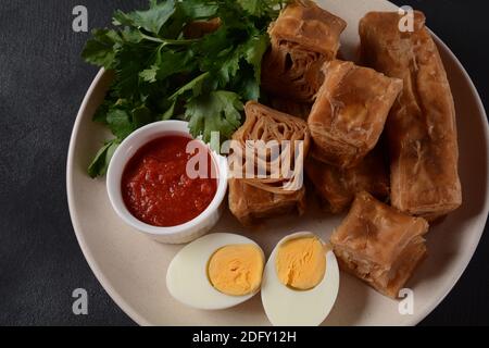 Jachnun oder Jahnun, jemenitisches jüdisches Gebäck, serviert mit frisch geriebenen Tomaten und gekochtem Ei und Zhug, aus den Adeni-Juden, und traditionell Stockfoto