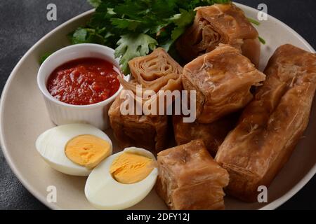 Jachnun oder Jahnun, jemenitisches jüdisches Gebäck, serviert mit frisch geriebenen Tomaten und gekochtem Ei und Zhug, aus den Adeni-Juden, und traditionell Stockfoto