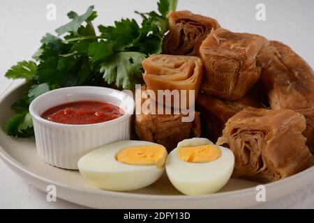 Jachnun oder Jahnun, jemenitisches jüdisches Gebäck, serviert mit frisch geriebenen Tomaten und gekochtem Ei und Zhug, aus den Adeni-Juden, und traditionell Stockfoto