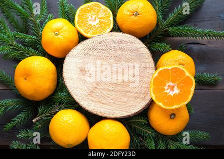 Neujahr Hintergrund auf runden Schnitt von Baum umgeben von Mandarinen, leben Tannenzweige und goldenen Lichtern Girlanden, mit Holz Platz für Text. Stockfoto