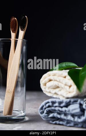 Bambus Zahnbürsten in Glas und Badetücher auf einem dunklen Hintergrund Stockfoto