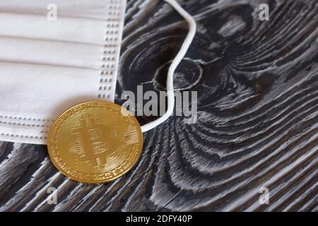 Bitcoin liegt auf einer medizinischen Maske. Auf Kiefernbrettern. Stockfoto