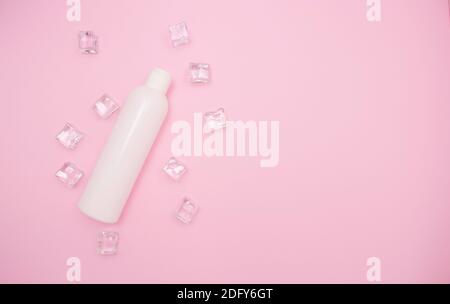 Weiße Plastikflasche für Shampoo oder andere Kosmetika. Eiswürfel um, rosa Hintergrund, freier Platz für Text, Draufsicht. Stockfoto