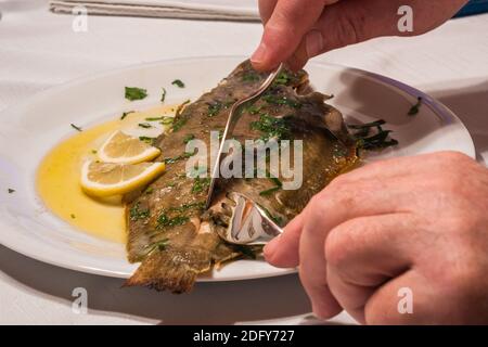 Filetieren oder Essen Sole Meuniere mit Braunbutter, Petersilie und Zitrone auf einem weißen Teller mit Gabel und Fischmesser Stockfoto