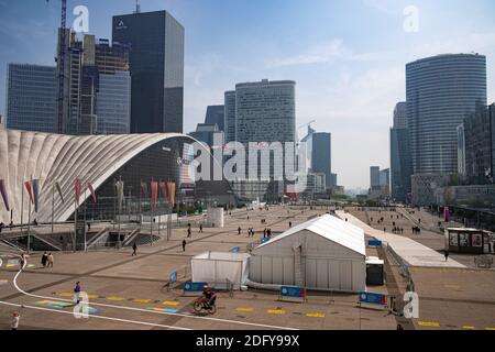 Menschen, die im Pariser Geschäftsviertel La Defense über die offene Fläche laufen. Der große Bogen der Verteidigung im Hintergrund. Aufgenommen am Mayday Holiday Stockfoto