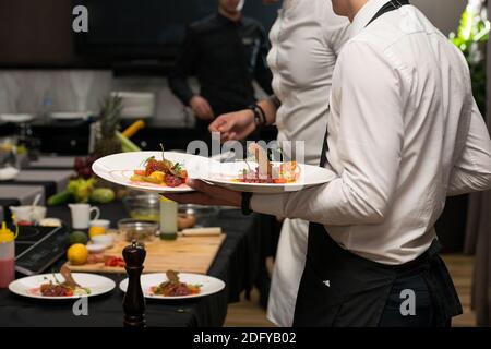 Der Kellner serviert das Gericht in einem Restaurant. Rindfleisch-Tartare mit verschiedenen Dip und Gemüse Stockfoto