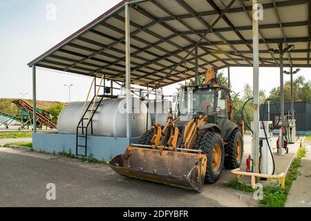 Gelber Traktor an der Tankstelle. Auffüllen. Schwere Ausrüstung. Tanks mit Kraftstoff. Stockfoto