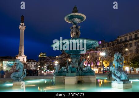 Beleuchteter Brunnen mit Säule von Pedro IV am Rossio Platz in Lissabon, Portugal. Aufgenommen während der Nacht Stockfoto