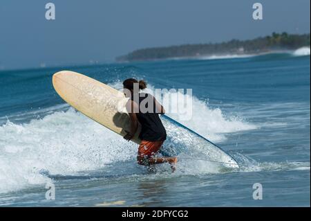 VARKALA, INDIEN - 14. März 2020: Ein indischer Mann läuft mit einem Surf Board auf die Welle zu. Stockfoto