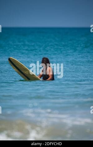 VARKALA, INDIEN - Mär 14, 2020: Ein indischer Mann sitzt auf seinem Surfbrett und sucht die Wellen. Stockfoto