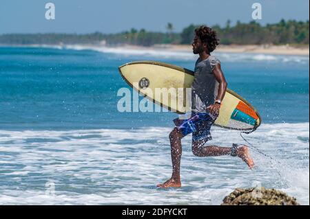 VARKALA, INDIEN - Mär 14, 2020: Ein indischer männlicher Surfer läuft furiousltowards the Ocean, um die Wellen zu fangen Stockfoto