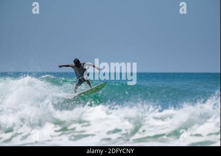 VARKALA, INDIEN - Mar 14, 2020: Ein indischer Surfer auf seinem Surfbrett zeigt seine Fähigkeiten in den Gewässern. Stockfoto