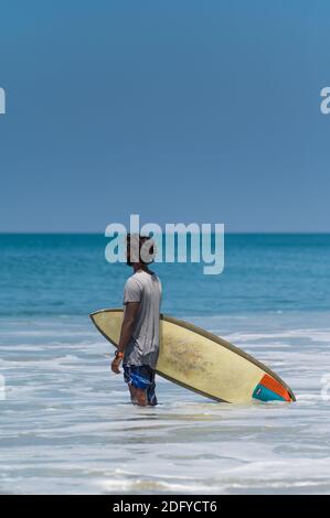 VARKALA, INDIEN - Mar 14, 2020: Ein indischer Mann mit seinem Surf Board wartet auf die Wellen im Ozean Stockfoto