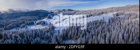 Atemberaubende Winterlandschaft mit schneebedeckten Bäumen und Wald, wie eine Straße durch die Landschaft schneidet. Stockfoto