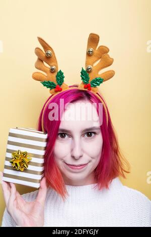 Mädchen in weißen Pullover und Hirsch Hörner auf dem Kopf, hält Geschenk in der Hand, gelber Hintergrund Stockfoto