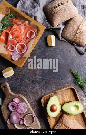 Draufsicht auf geräucherte Lachsscheiben mit Zwiebel, Dill, Zitrone und Avocado auf einem Tisch mit Kopierfläche. Stockfoto