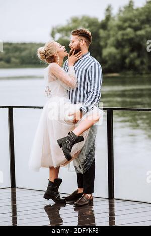 Die Braut und Bräutigam zärtlich umarmt stehen sie und posieren auf dem Pier. Stockfoto