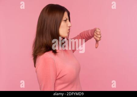 Profil Porträt äußerst unzufrieden Frau mit braunen Haaren in rosa Pullover zeigt Daumen nach unten, nicht mögen und nicht mit Informationen, Konflikt. Zoll Stockfoto